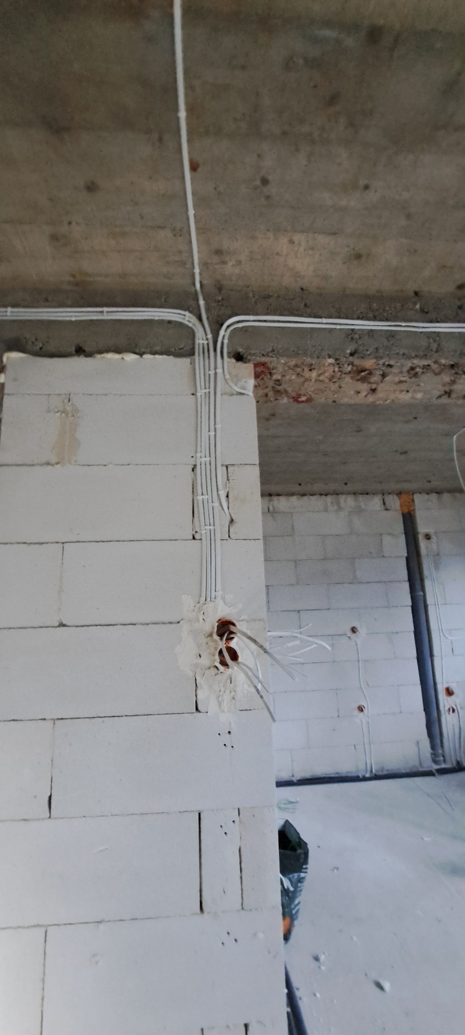 Wewnętrzne okablowanie elektryczne w surowym stanie, białe kable prowadzone po ścianie z betonu komórkowego i pod sufitem, widoczne puszki instalacyjne z wystającymi przewodami.