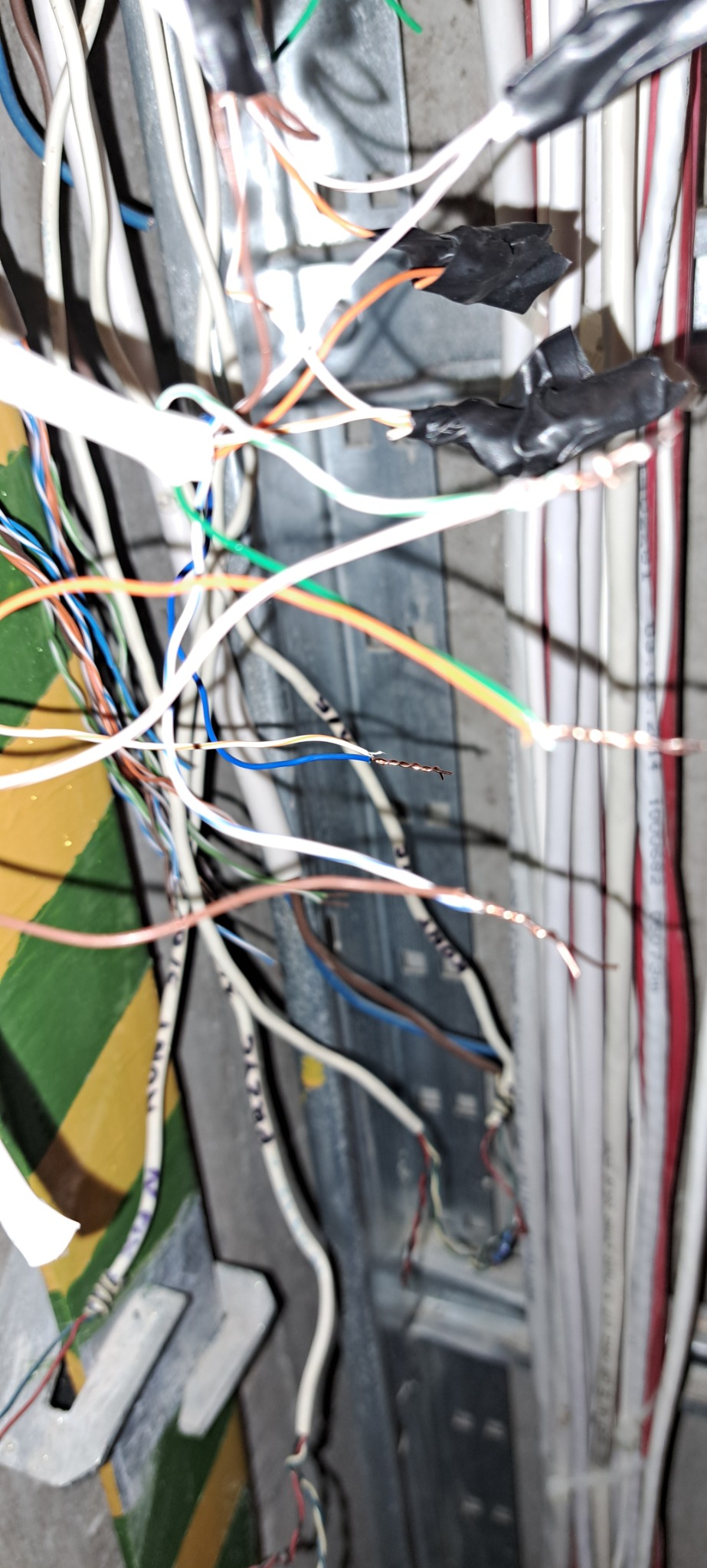 Skomplikowana sieć przewodów elektrycznych o różnych kolorach, niektóre z zaizolowanymi połączeniami, widoczne w metalowej obudowie, sugerujące etap instalacji lub naprawy.