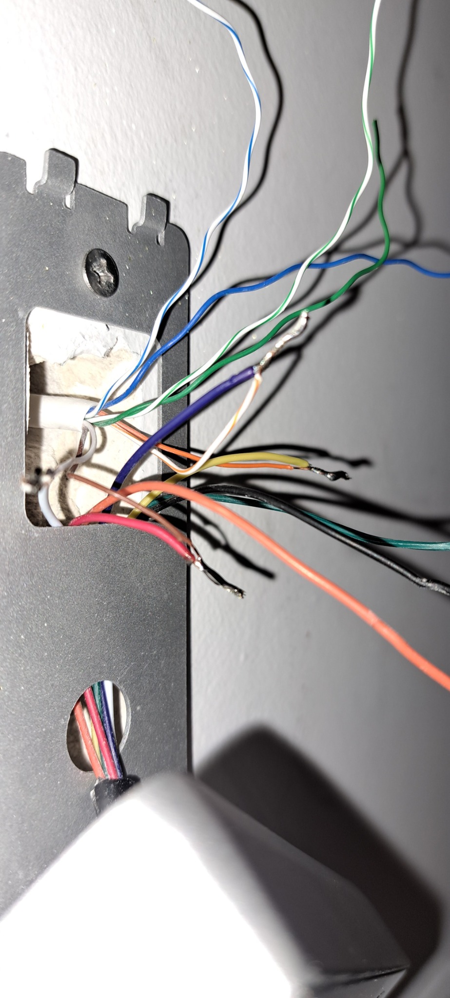 Szczegółowe ujęcie przewodów elektrycznych różnego koloru wychodzących z otworu w ścianie, zamocowanych do metalowej płytki montażowej, z widocznymi końcówkami kabli przygotowanymi do podłączenia.