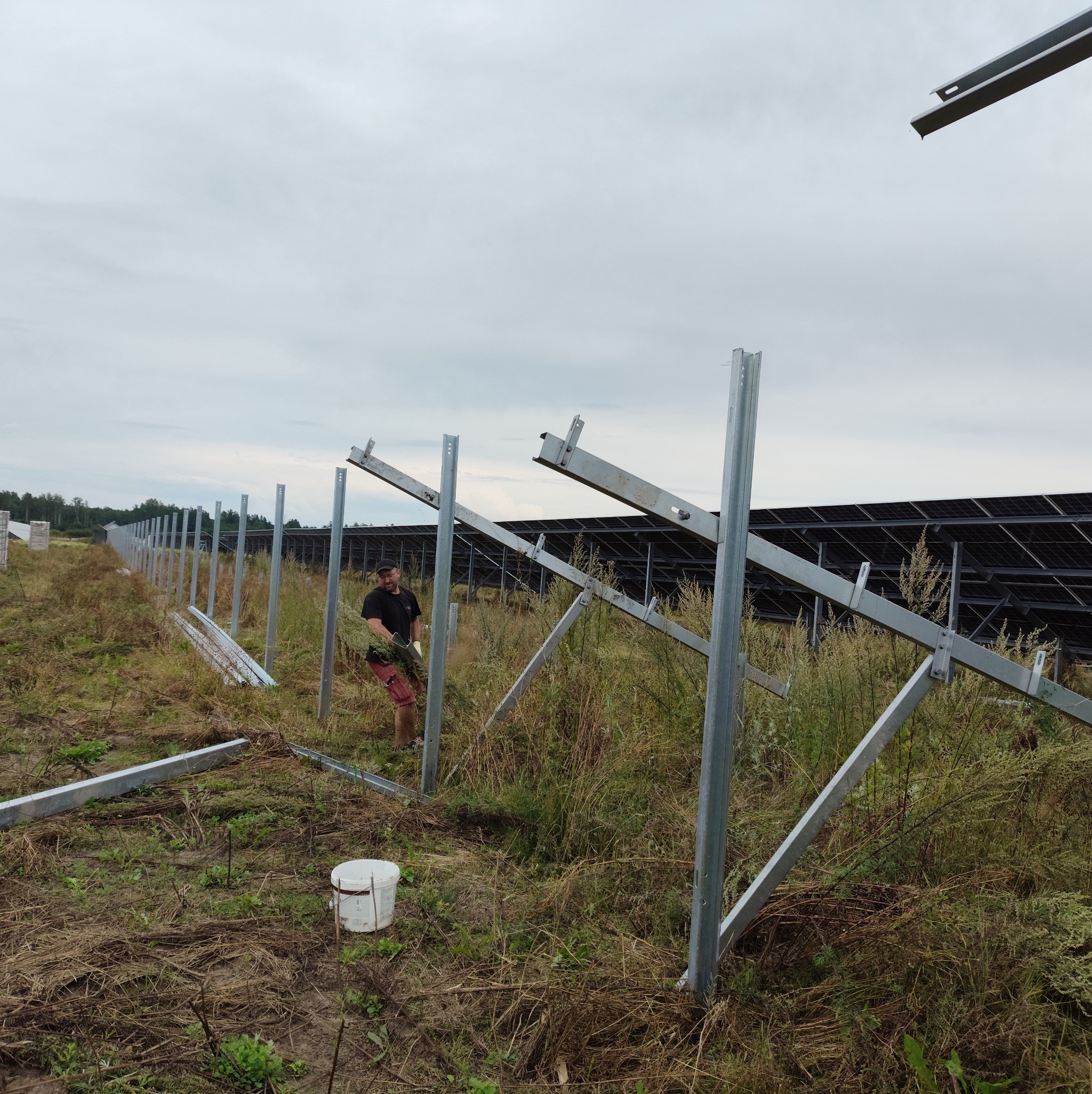 Montaż konstrukcji wsporczej pod panele słoneczne na zewnątrz. Widoczne metalowe profile i częściowo zainstalowane panele w tle. Prace montażowe w toku.