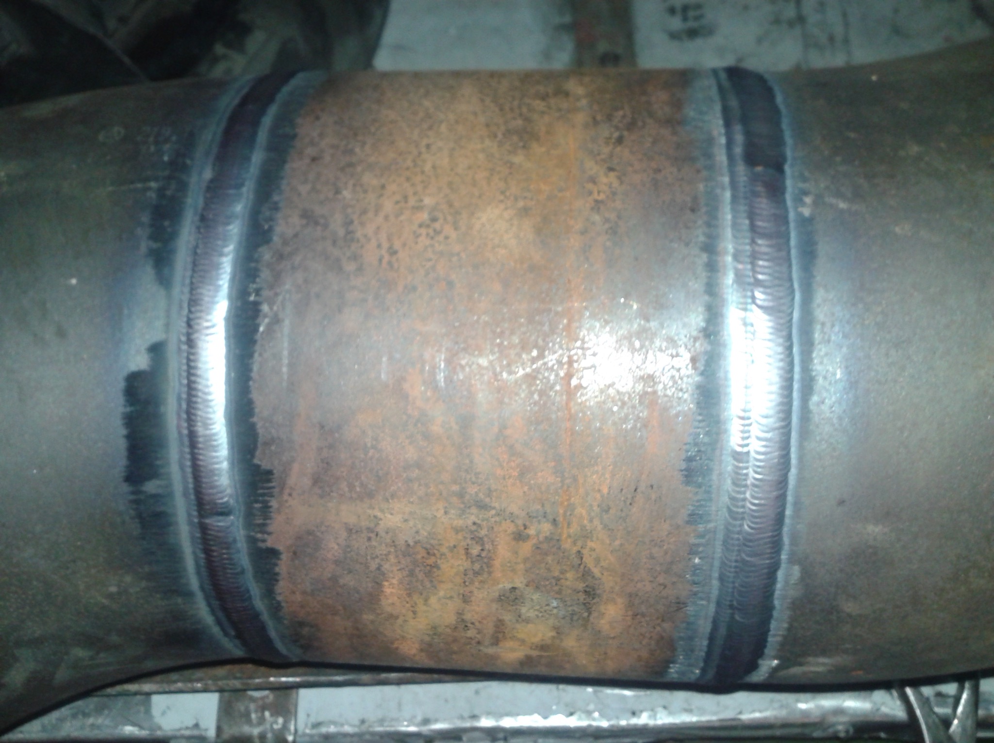 Spoina na rurze stalowej, widoczne ślady rdzy i niedoskonałości spoiny, surowy stan techniczny.