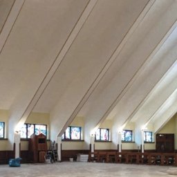 AGWA Sp. z o.o. - Wnętrze kościoła w trakcie prac wykończeniowych, widoczne świeżo pomalowane ściany i sufit, okna witrażowe, rusztowania i sprzęt malarski.