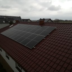 AGWA Sp. z o.o. - Panele słoneczne zamontowane na brązowym, spadzistym dachu domu jednorodzinnego, widok z góry na tle pochmurnego nieba.