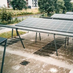 AGWA Sp. z o.o. - Zadaszenie parkingu z panelami fotowoltaicznymi, widok z góry na szarą kostkę brukową i zaparkowany czarny samochód.