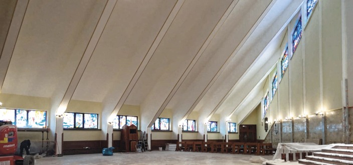 Wnętrze kościoła w trakcie prac wykończeniowych, widoczne świeżo pomalowane ściany i sufit, okna witrażowe, rusztowania i sprzęt malarski.