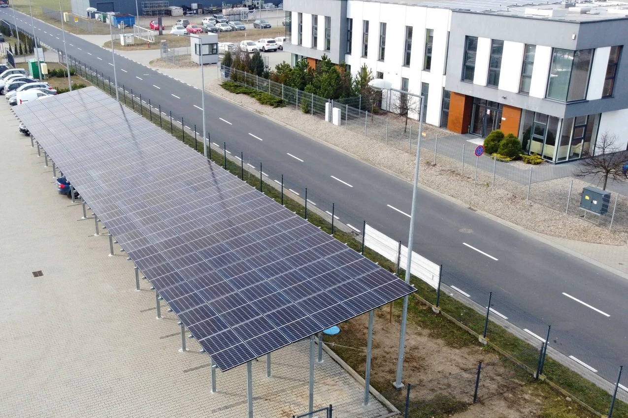 Zadaszenie parkingu wykonane z paneli fotowoltaicznych, widok z góry na duży parking przy budynku biurowym.