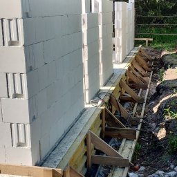 R-PRO KAROLINA RURARZ - Budowa domu z bloczków betonu komórkowego. Widoczne szalunki fundamentowe i początek wznoszenia ścian. W tle drzewa.