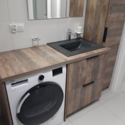 STOLARSTWO PAWEŁ KOPACZEWSKI - Łazienka z pralką zabudowaną pod blatem z umywalką i szafką w kolorze drewna, białe płytki na ścianach, minimalistyczny design.