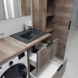 STOLARSTWO PAWEŁ KOPACZEWSKI - Łazienka z zabudową meblową: umywalka nablatowa w kolorze czarnym, drewnopodobny blat, pralka pod blatem, szafka z otwartymi szufladami i półkami.