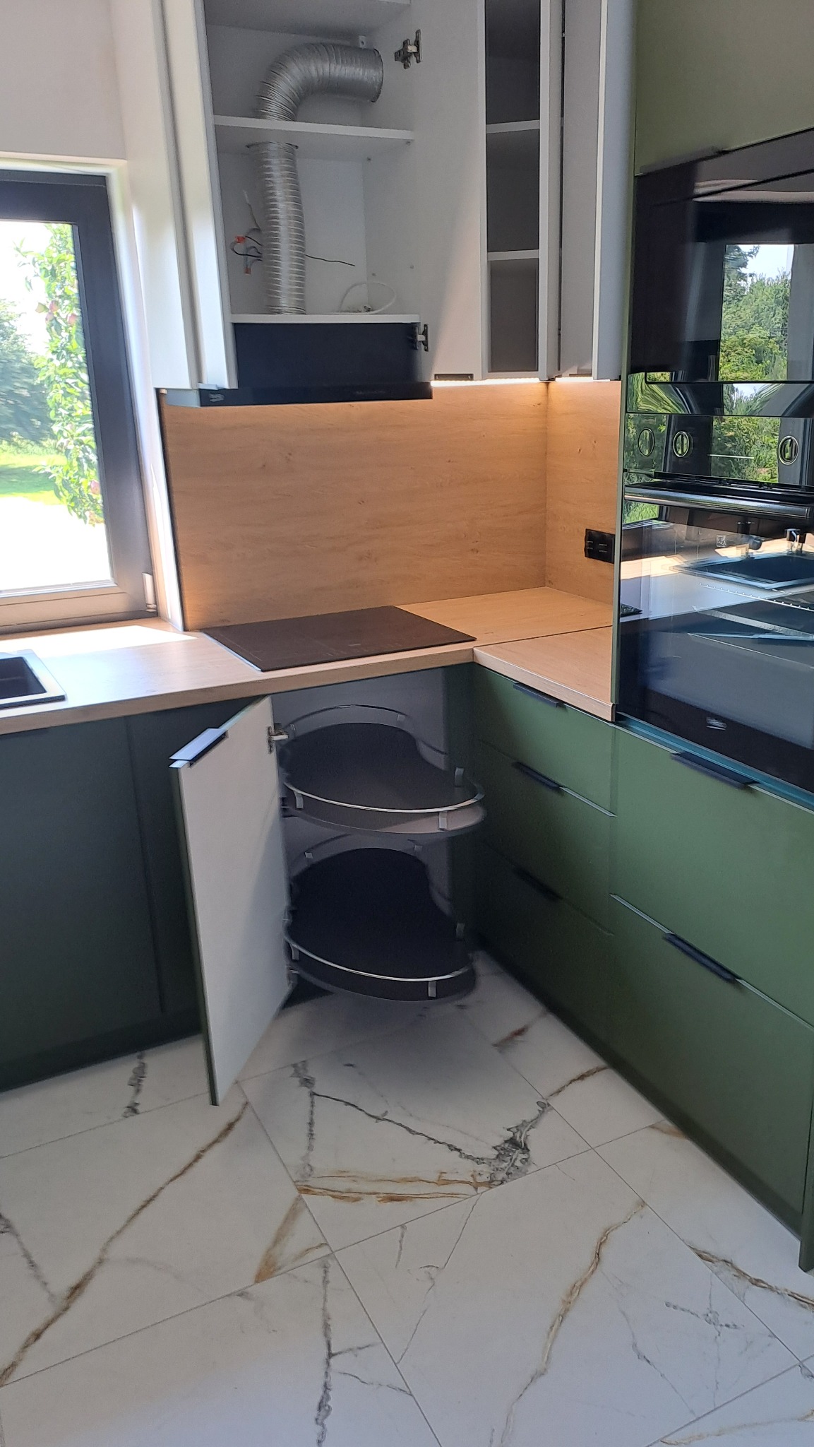 Nowoczesna kuchnia z zielonymi frontami, systemem cargo w szafce narożnej i płytą indukcyjną na blacie.