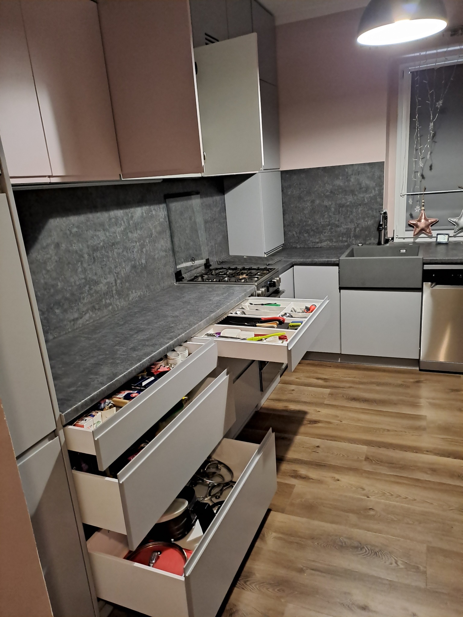 Szare meble kuchenne na wymiar z otwartymi szufladami, widoczny organizer na sztućce, garnki i produkty spożywcze.