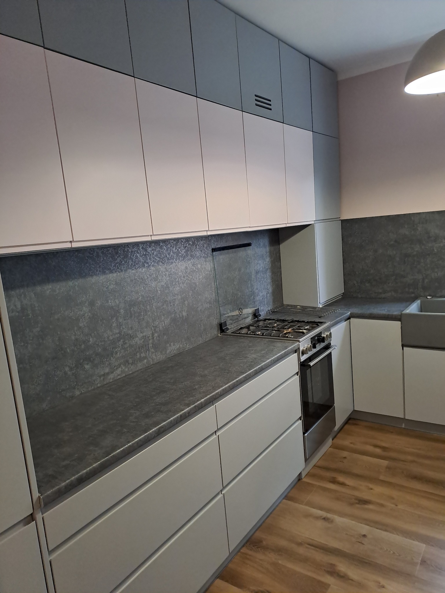 Nowoczesna kuchnia z szarymi i białymi frontami szafek, blatem imitującym beton oraz drewnianą podłogą.