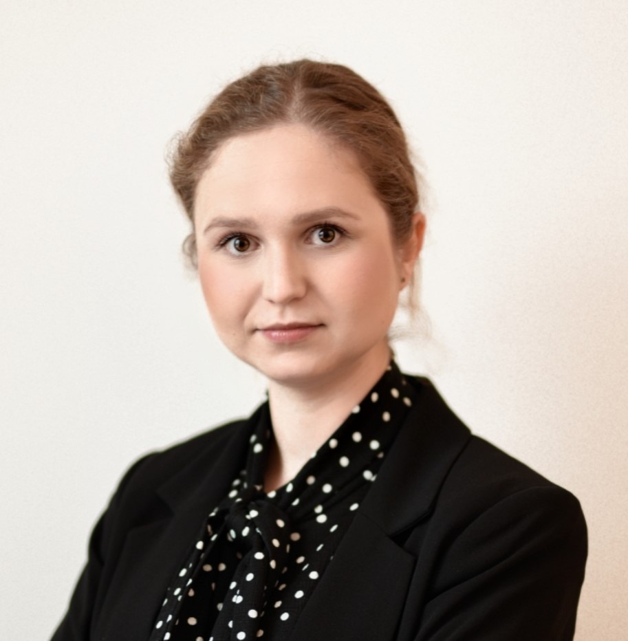 Portret kobiety w czarnym żakiecie i bluzce w białe kropki na jasnym tle.