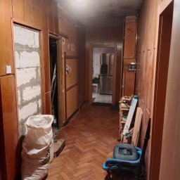 Korytarz w początkowej fazie remontu. 
Jedne z drzwi zamurowane.
Montaż płyt gk, sufitu podwieszanego, szpachlowanie, renowacja parkietu dębowego,   montaż lamp, malowanie ścian i sufitu.
