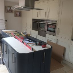 MJ Serwis - Montaż wyspy kuchennej z narzędziami: poziomica, wkrętarka, kartonowe opakowanie leżące obok szafek.