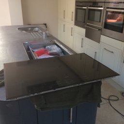 MJ Serwis - Montaż płyty indukcyjnej AEG w blacie kuchennym, widoczne narzędzia i poziomica, białe szafki w tle.