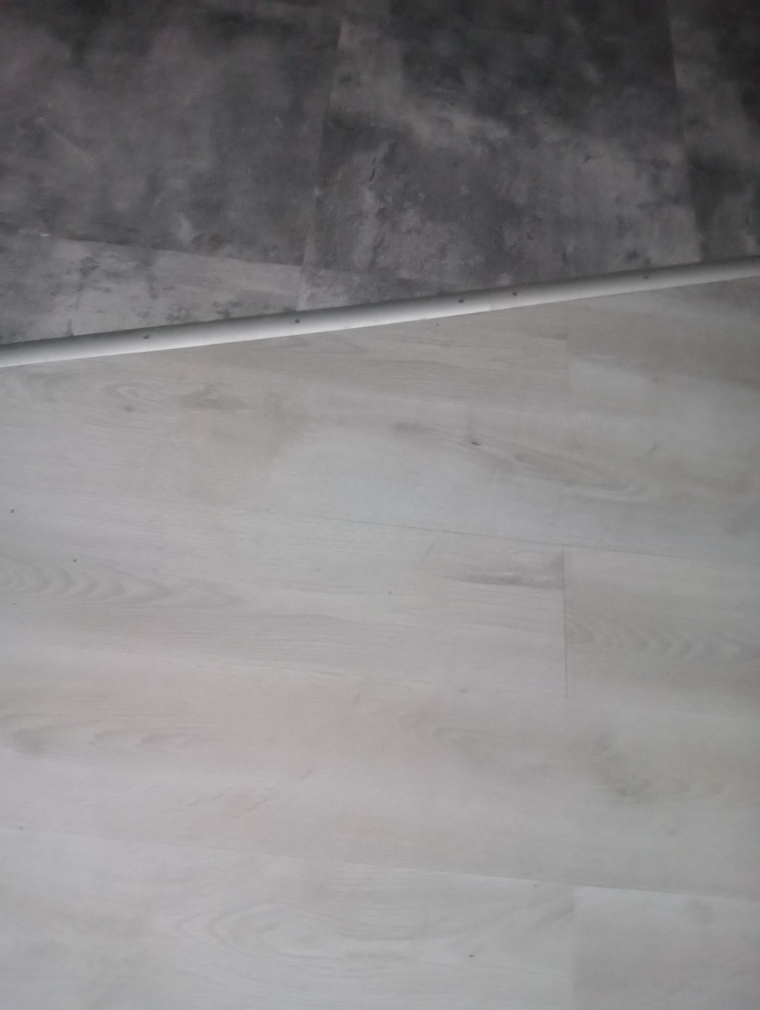 Świeżo ułożone, jasne panele podłogowe w Protasy, z widoczną listwą przypodłogową i fragmentem szarej ściany.