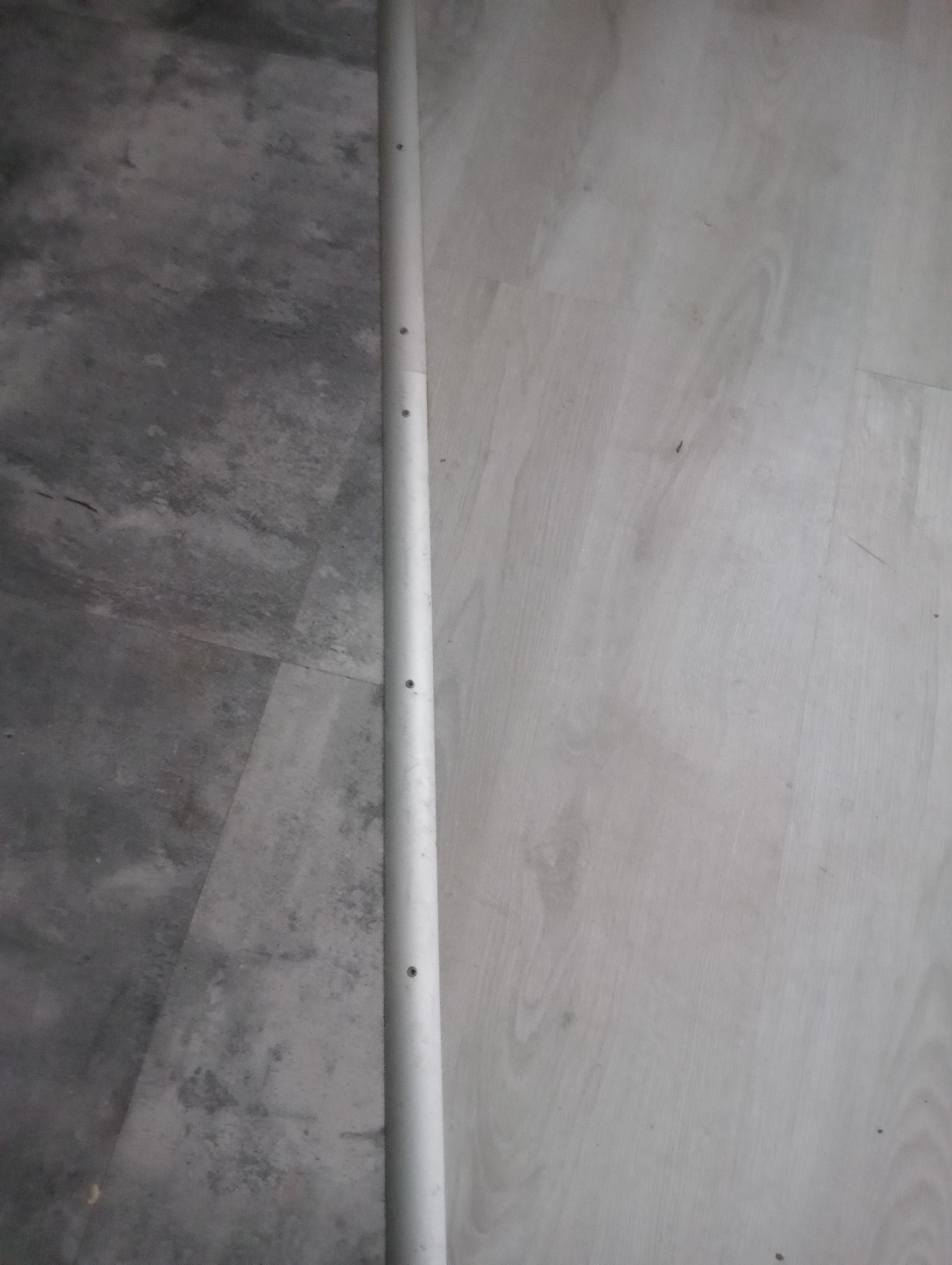 Szara podłoga z widoczną listwą przypodłogową z otworami montażowymi.