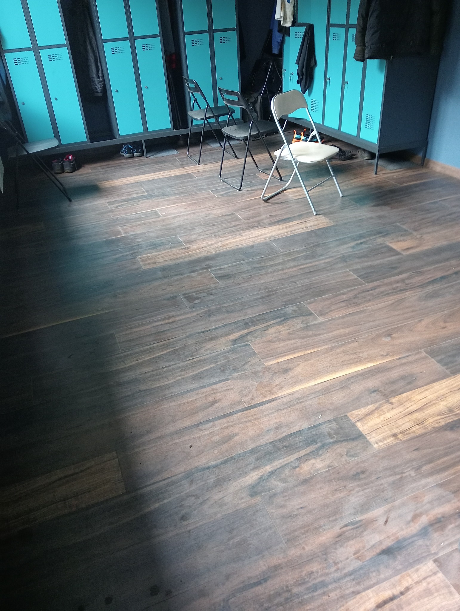 Nowa podłoga z paneli imitujących drewno, ułożona w szatni z niebieskimi szafkami i krzesłami.