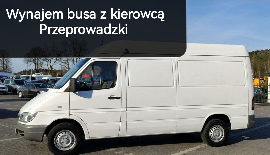 Biały samochód dostawczy typu furgon na parkingu, potencjalnie do transportu lub przeprowadzki, z widocznymi innymi pojazdami w tle.