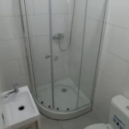 Nowoczesna łazienka z kabiną prysznicową narożną, umywalką z szafką i toaletą, wykończona białymi płytkami na ścianach i szarą podłogą.