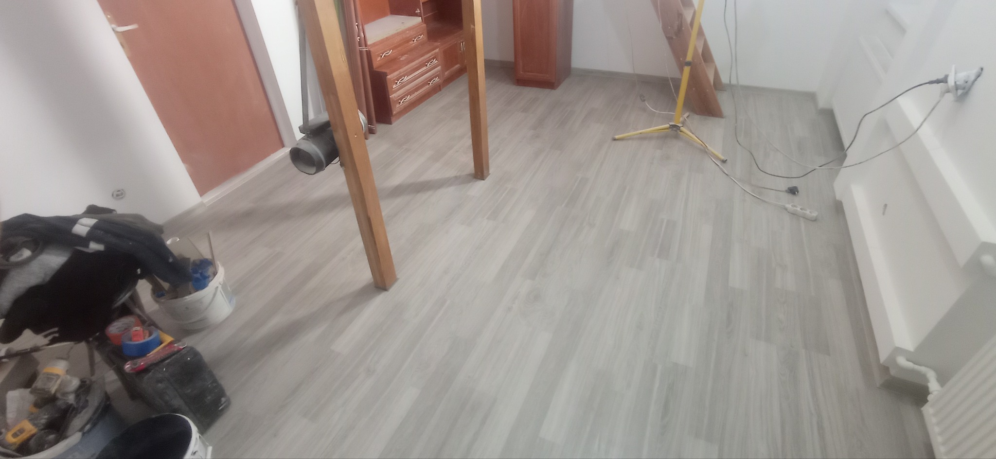 Świeżo położona, jasnoszara podłoga laminowana w pokoju podczas prac wykończeniowych, widoczny sprzęt malarski, drabina i lampa halogenowa