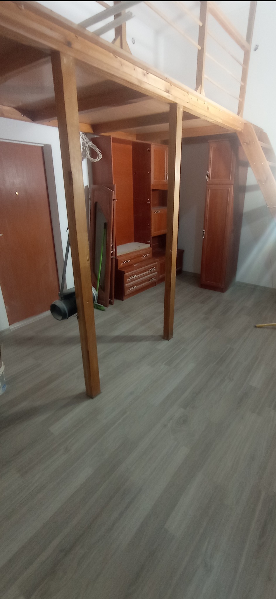 Wnętrze pokoju z drewnianą antresolą na konstrukcji z belek, pod którą znajdują się brązowe szafy i komody, a na podłodze panele imitujące drewno.