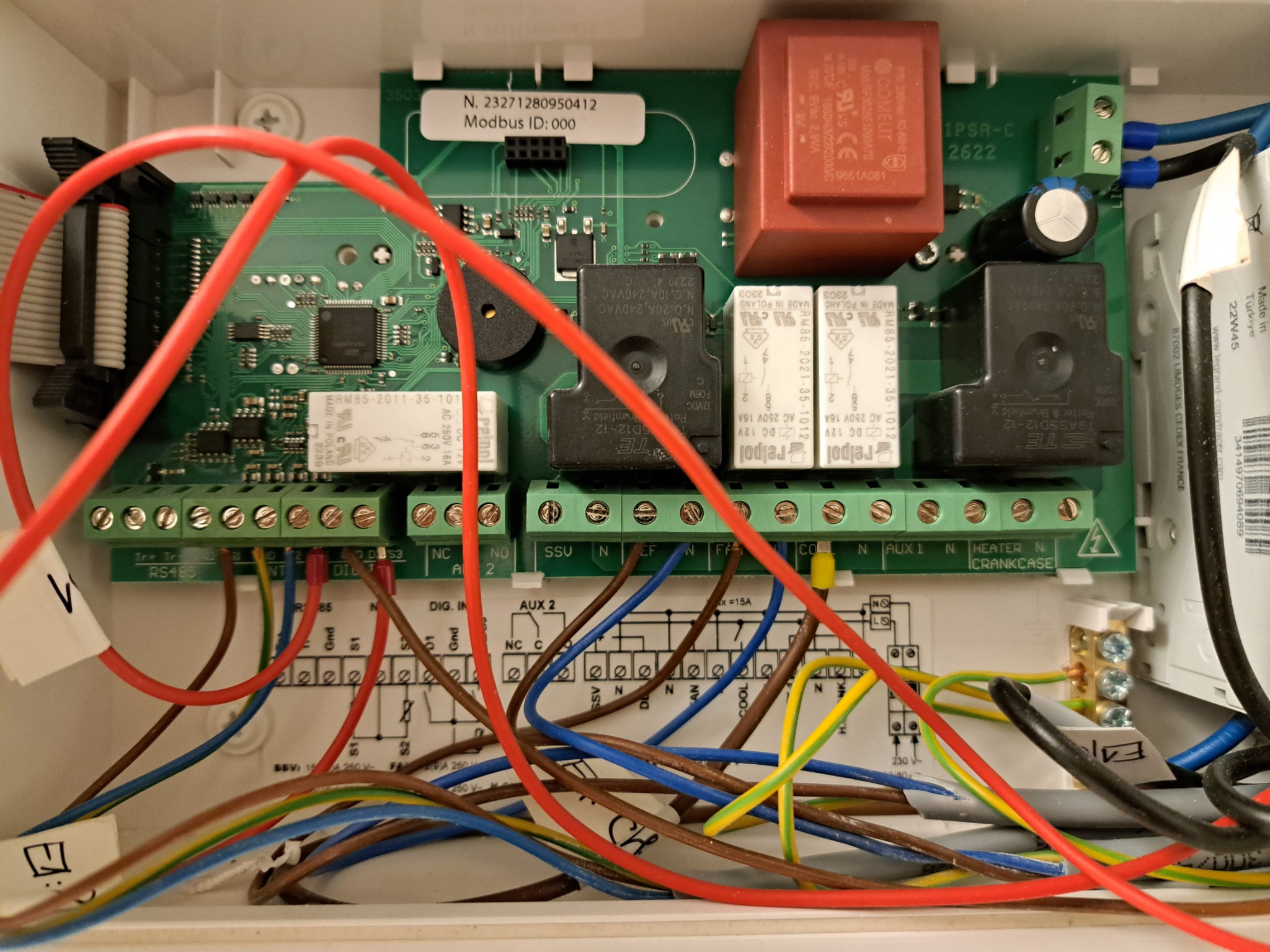 Otwarta obudowa z widoczną płytą sterującą z licznymi przewodami, złączkami i elementami elektronicznymi, w tym przekaźnikami Relpol i transformatorem Comelit IPSA-C 2622, z etykietą Modbus ID: 000