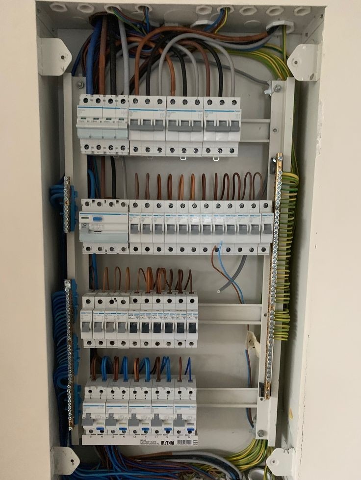 Rozdzielnica elektryczna z widocznymi bezpiecznikami, przewodami i listwą zaciskową, zamontowana w białej obudowie w ścianie.