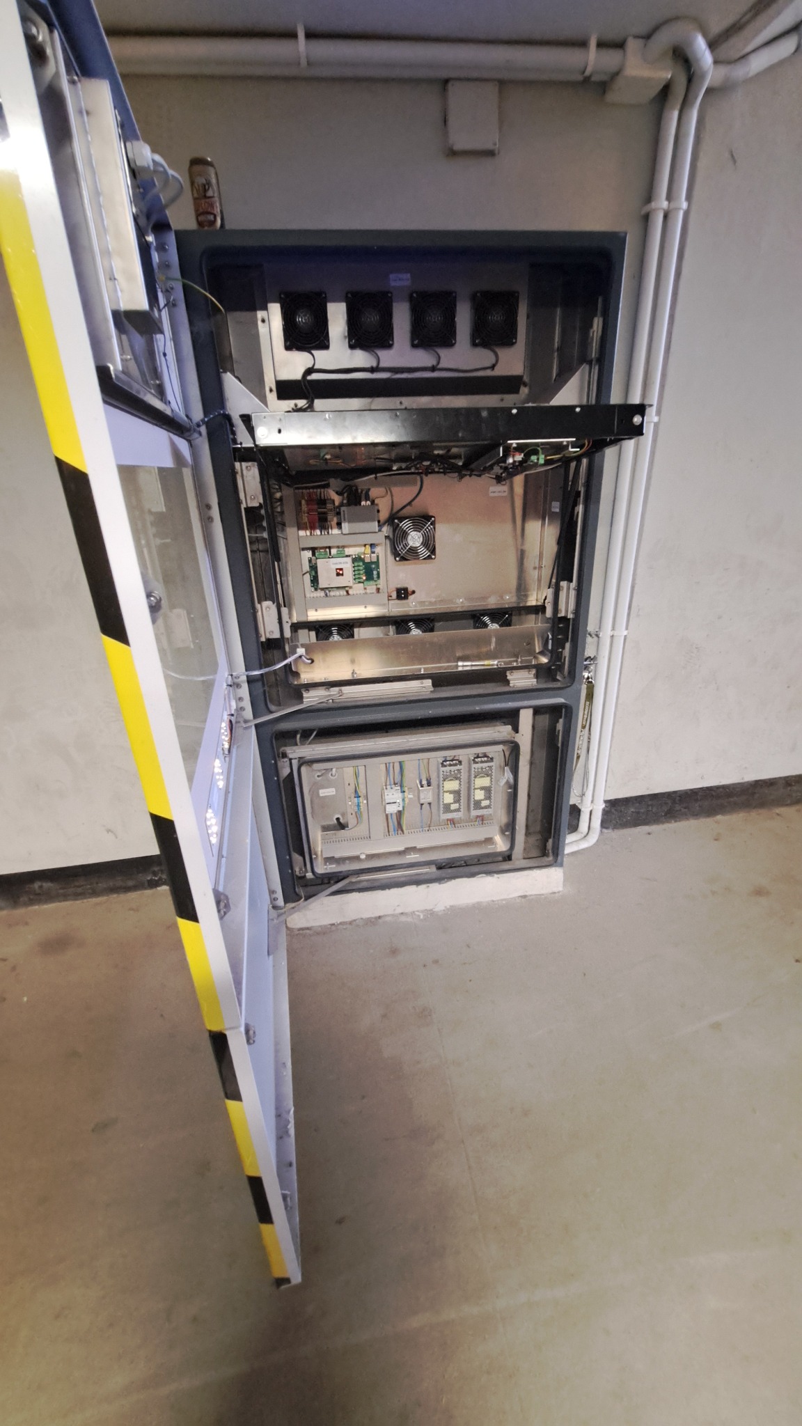 Otwarta szafa sterownicza z widocznymi modułami elektronicznymi, wentylatorami i okablowaniem w pomieszczeniu technicznym.