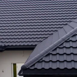 Szczeg&oacute;łowe ujęcie czarnego dachu z blachodach&oacute;wki modułowej firmy Venecja, z widocznymi rynnami i elementami wykończeniowymi, na tle jasnej elewacji domu.
