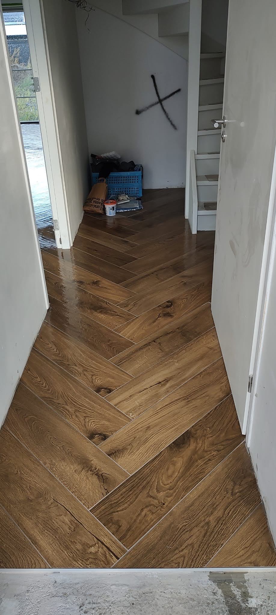 Ułożona podłoga z paneli w jodełkę w trakcie prac wykończeniowych, widoczne niedoskonałości i przygotowanie do dalszych prac.