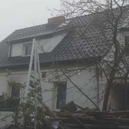 Aesthetics - Dom z dachem pokrytym szarą dachówką, widoczne rusztowanie i sterta starych desek na pierwszym planie, pochmurna pogoda.