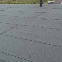 Aesthetics - Szary dach pokryty papą termozgrzewalną z widocznym kominem wentylacyjnym na tle miejskiego krajobrazu z budynkami i zielenią.