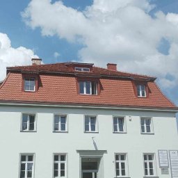 Aesthetics - Dwupiętrowy budynek z czerwonym dachem z dachówki ceramicznej, widoczne okna dachowe, elewacja w kolorze złamanej bieli, zabezpieczone wejście taśmą ostrzegawczą.