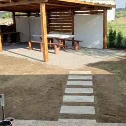 Kris - Zadaszona altana z grillem i stołem piknikowym w ogrodzie w Zielonej Górze, z płytkami imitującymi kamień na tarasie i ścieżką z betonowych płyt.
