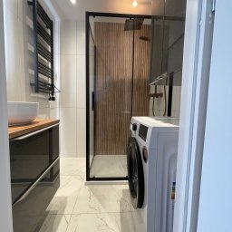 Kris - Nowoczesna łazienka z kabiną prysznicową typu walk-in z drewnianym panelem, umywalką nablatową i czarnym grzejnikiem drabinkowym. Marmurowe płytki podłogowe.