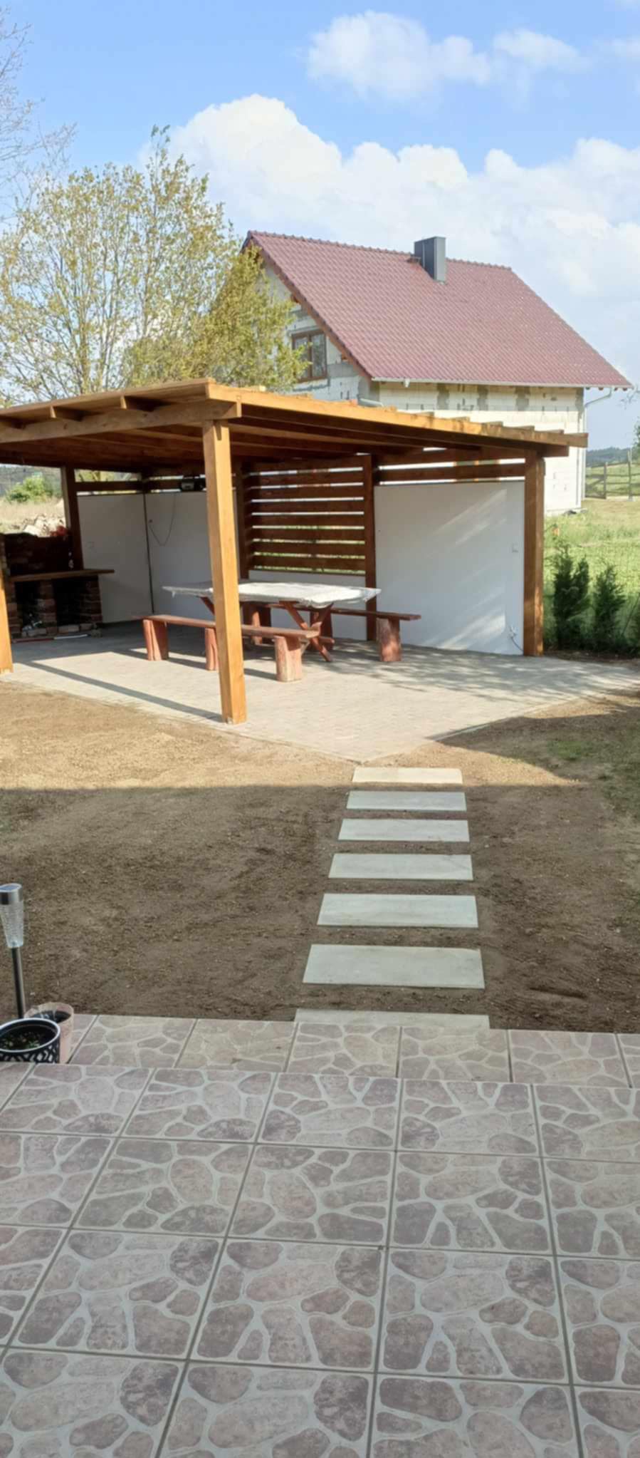 Zadaszona altana z grillem i stołem piknikowym w ogrodzie w Zielonej Górze, z płytkami imitującymi kamień na tarasie i ścieżką z betonowych płyt.