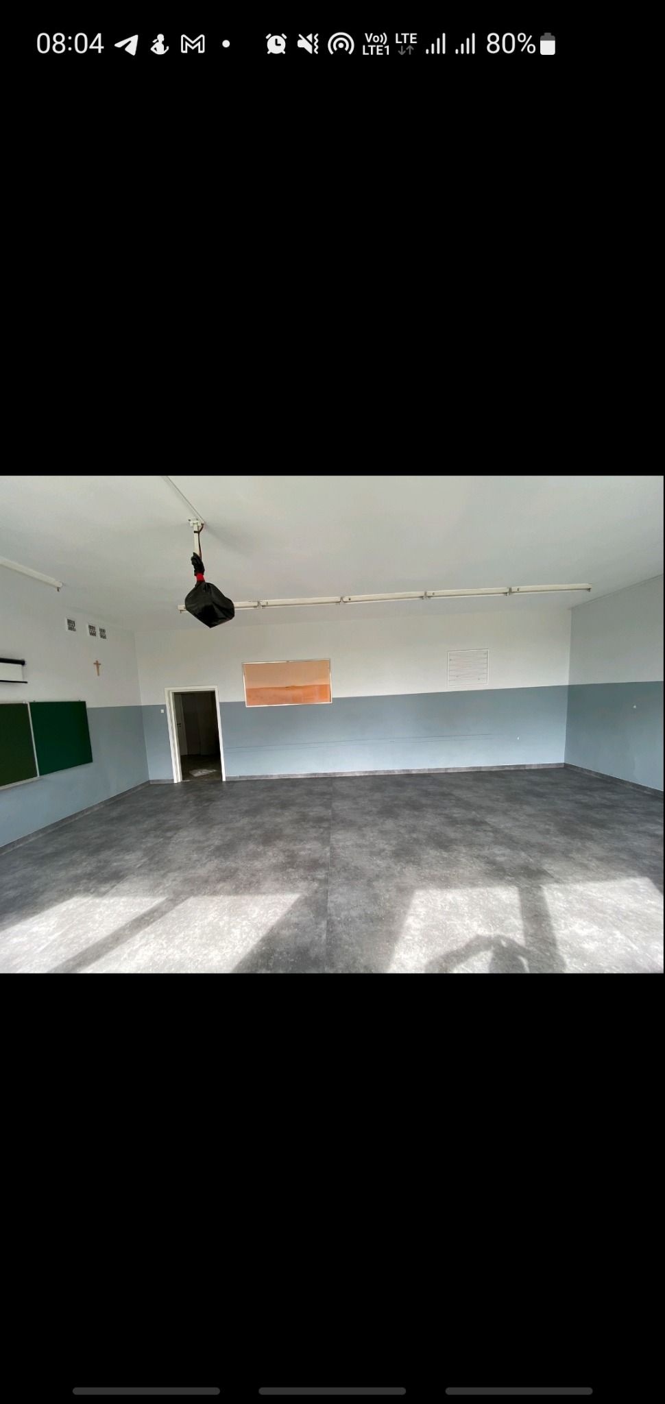 Szara wykładzina ułożona w przestronnym, jasnym pomieszczeniu z widocznym projektorem wiszącym u sufitu i zieloną tablicą.