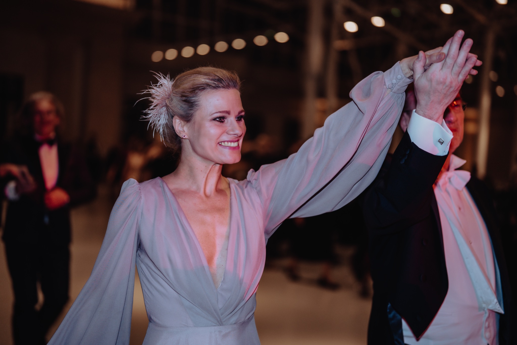 Elegancka kobieta w balowej sukni tańczy z mężczyzną w smokingu, oświetlenie punktowe w tle.