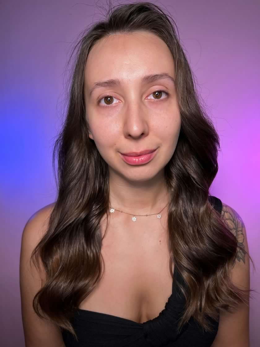 Portret kobiety przed wykonaniem upiększania twarzy, widoczne brwi przed regulacją i delikatny uśmiech, tło fioletowo-niebieskie.