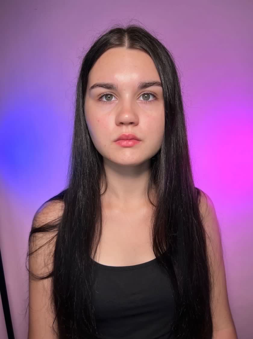 Portret młodej kobiety z długimi, ciemnymi włosami i delikatnym, naturalnym wyglądem, na tle z gradientem od różu do fioletu.