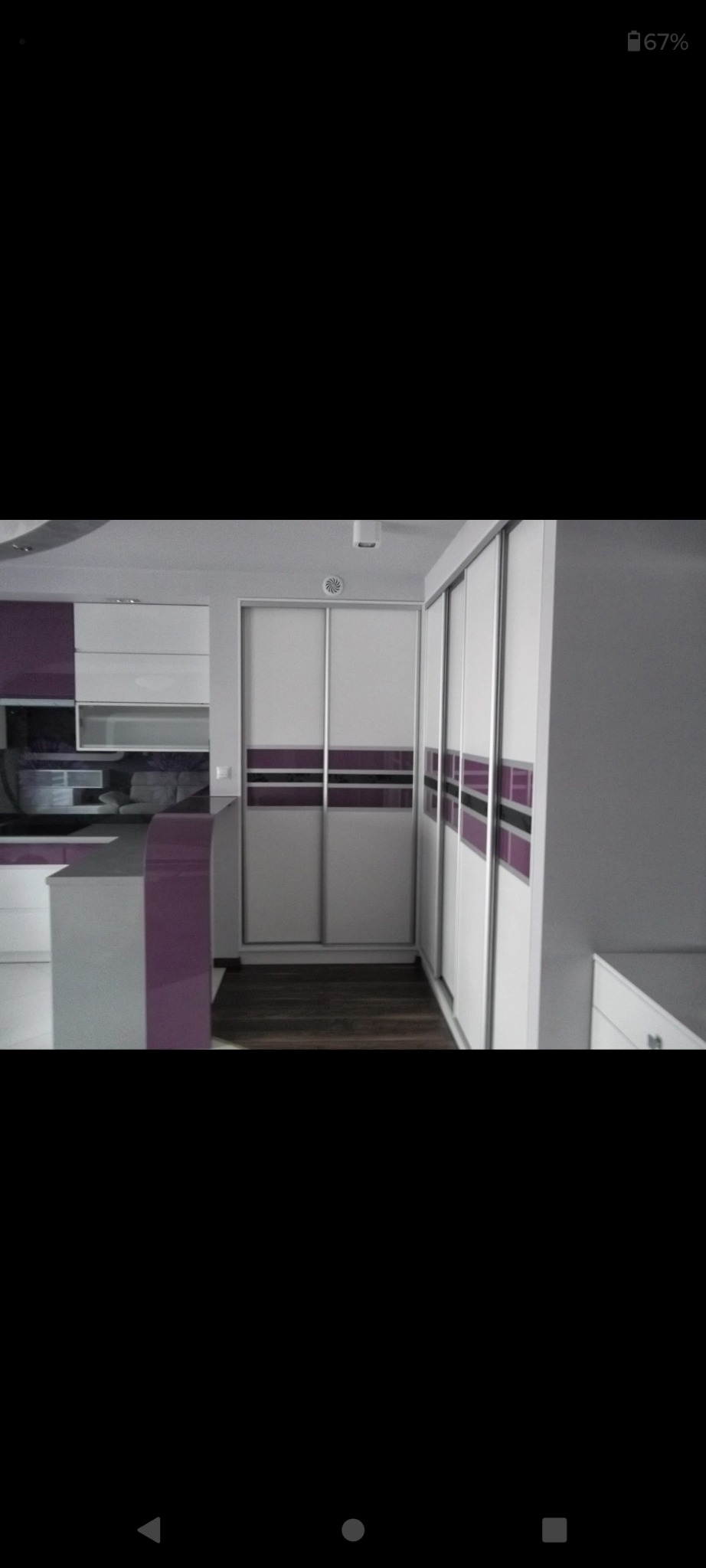 Nowoczesna zabudowa kuchenna z szafkami w kolorze białym i fioletowym, z przesuwnymi drzwiami szafy wnękowej z fioletowymi akcentami, na podłodze ciemne panele.