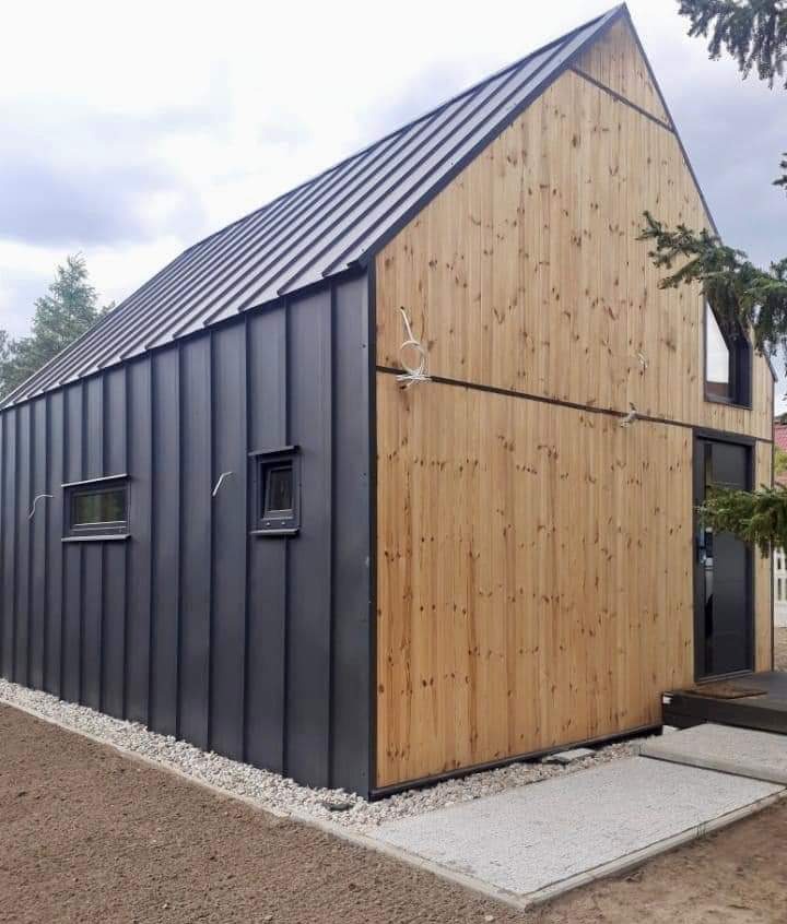 Nowoczesny dom z dwukolorową elewacją: grafitowa blacha trapezowa i jasne drewno, widoczne okna i drzwi, otoczenie z kamiennego żwiru.