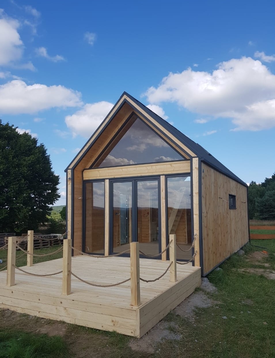 Nowoczesny, drewniany dom z dużymi przeszkleniami w Rzeszowie, z tarasem zabezpieczonym liną jutową, na tle błękitnego nieba z obłokami.