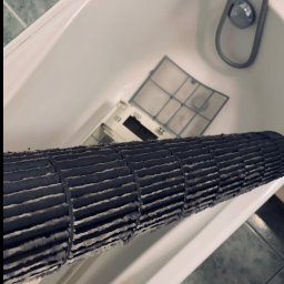 JohnnyKlima JAN GAJEWSKI - Brudny, cylindryczny filtr klimatyzacji w wannie, obok kratka filtra. Widoczne osady kurzu i zanieczyszczeń. Konieczność serwisu.