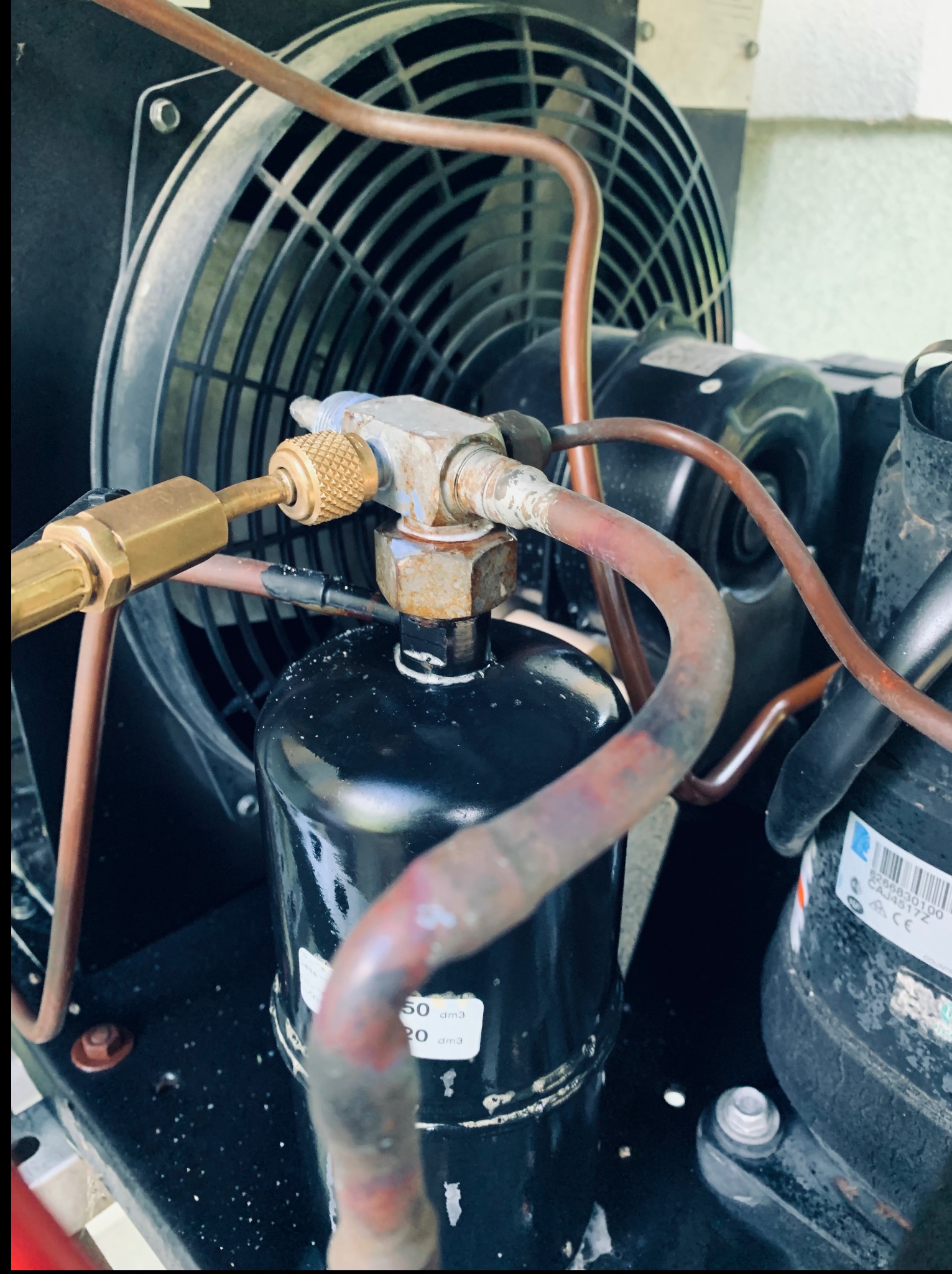 Detal klimatyzacji przemysłowej: wentylator, rury miedziane i czarny filtr. Widoczne złącza i naklejki z oznaczeniami technicznymi. Oświetlenie naturalne, kadr z bliska.