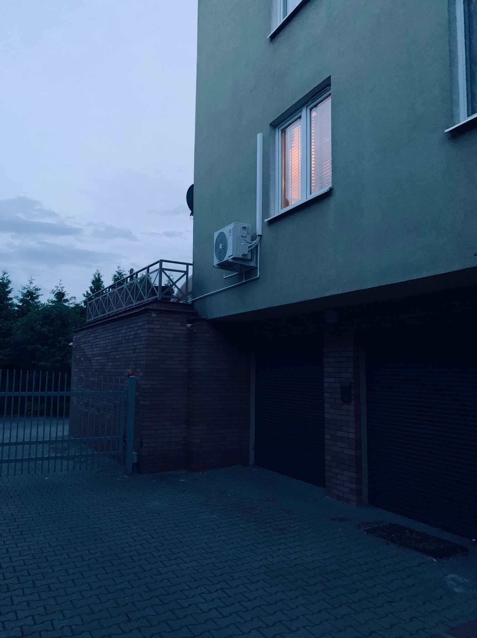 Zamontowany klimatyzator na ścianie budynku mieszkalnego o zmierzchu, z widocznym oświetleniem wewnątrz. Widok z zewnątrz na jednostkę klimatyzacyjną.