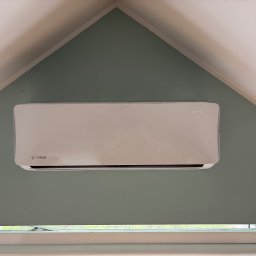 Hydrosław Sławomir Wojtalik - Biały klimatyzator Rotenso zamontowany na zielonej ścianie pod skośnym sufitem, widok z dołu, okno w tle.