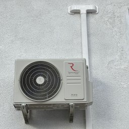 Hydrosław Sławomir Wojtalik - Zamontowana jednostka zewnętrzna klimatyzacji Rotenso Hiro Series na teksturowanej, jasnej ścianie budynku z widocznymi wspornikami i odprowadzeniem skroplin.